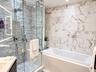 Walk-in glass-enclosed shower with stacked stone tiling, built-in soaking tub featuring a decorative stone-patterned wall surround, and a backlit vani