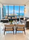 Floor-to-ceiling windows featuring panoramic water and city scenery, reflective polished tile flooring, and multi-light linear pendant lighting