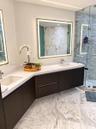 Floating dual vanity featuring dark cabinetry, solid-surface countertops, integrated rectangular sinks, and large, illuminated mirrors, complete with 