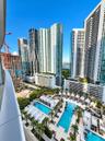 Curved glass balcony railing overlooking an expansive multi-level pool deck with integrated cabanas, palm landscaping, and surrounding metropolitan hi