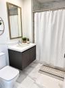 Floating vanity with a quartz countertop, rectangular sink, gold-framed mirror, and large-format tile flooring