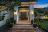 Exterior entrance featuring painted brick pillars, double front doors with an arched glass transom, stone step entry, and wall-mounted light fixtures
