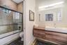 Floating wood-finish vanity with a rectangular integrated sink, wall-mounted rectangular mirror, shower enclosure featuring a glass sliding door, and 