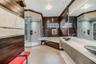 Custom bathroom featuring wood-paneled walls, a glass-enclosed shower, a jetted soaking tub, floating vanity with dual glass vessel sinks, and light-t