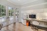 Custom built-in desk with integrated storage cabinetry, wood-finish flooring, and white paneled walls featuring multi-pane glass doors