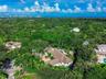 Aerial perspective featuring a multi-gabled roofline, a circular paved driveway, a private swimming pool, and extensive mature landscaping on a heavil