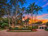 Circular brick paver driveway, mature landscaping with palm trees, and multi-car garage