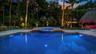 In-ground swimming pool with integrated elevated spa, stone-paver decking, thatch-roof cabana, and mature perimeter landscaping