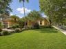 Single-story exterior featuring a tile roof, paved driveway, stucco facade, and mature landscaping