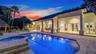 Spacious exterior featuring a covered patio with columns, stone-paved decking, a built-in swimming pool, a separate spa, and multiple sets of French d