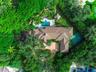 Aerial perspective of a sprawling property featuring a paved circular driveway, a swimming pool with spa, a tennis court, and mature perimeter landsca