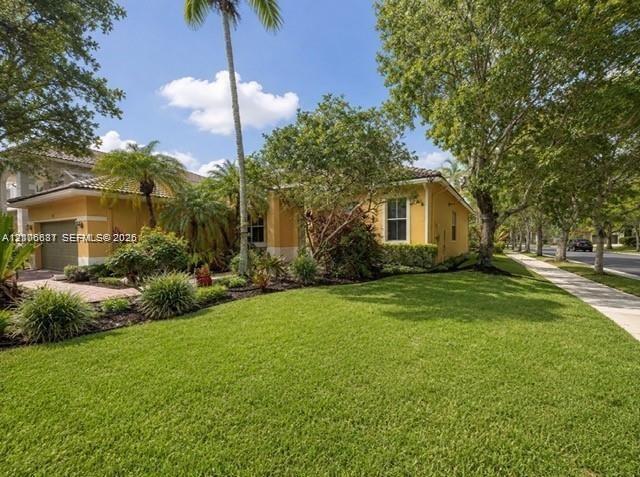 Single-story exterior featuring a tile roof, paved driveway, stucco facade, and mature landscaping