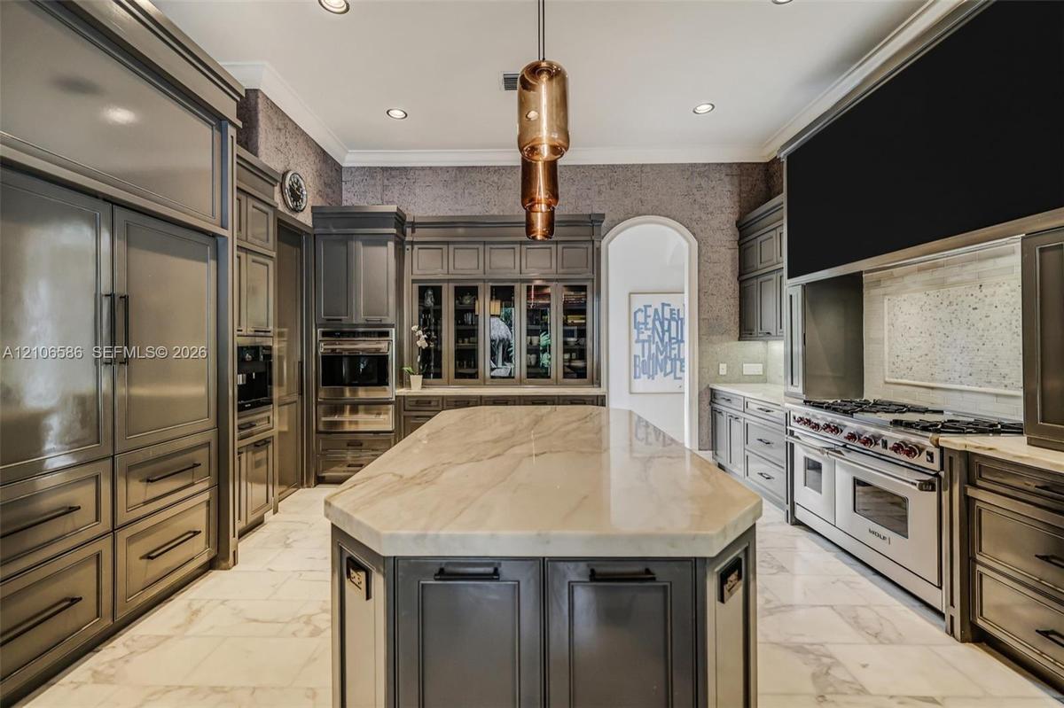Custom cabinetry with integrated appliances, expansive central island with stone-finish countertop, professional-grade range, built-in display cabinet
