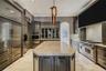 Custom cabinetry with integrated appliances, expansive central island with stone-finish countertop, professional-grade range, built-in display cabinet