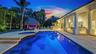Custom swimming pool with integrated spa, expansive stone patio, covered lanai featuring structural columns, and a thatched-roof cabana