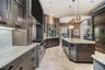 Kitchen featuring custom cabinetry, light-toned stone countertops, professional-grade range, large central island, and stone tile flooring