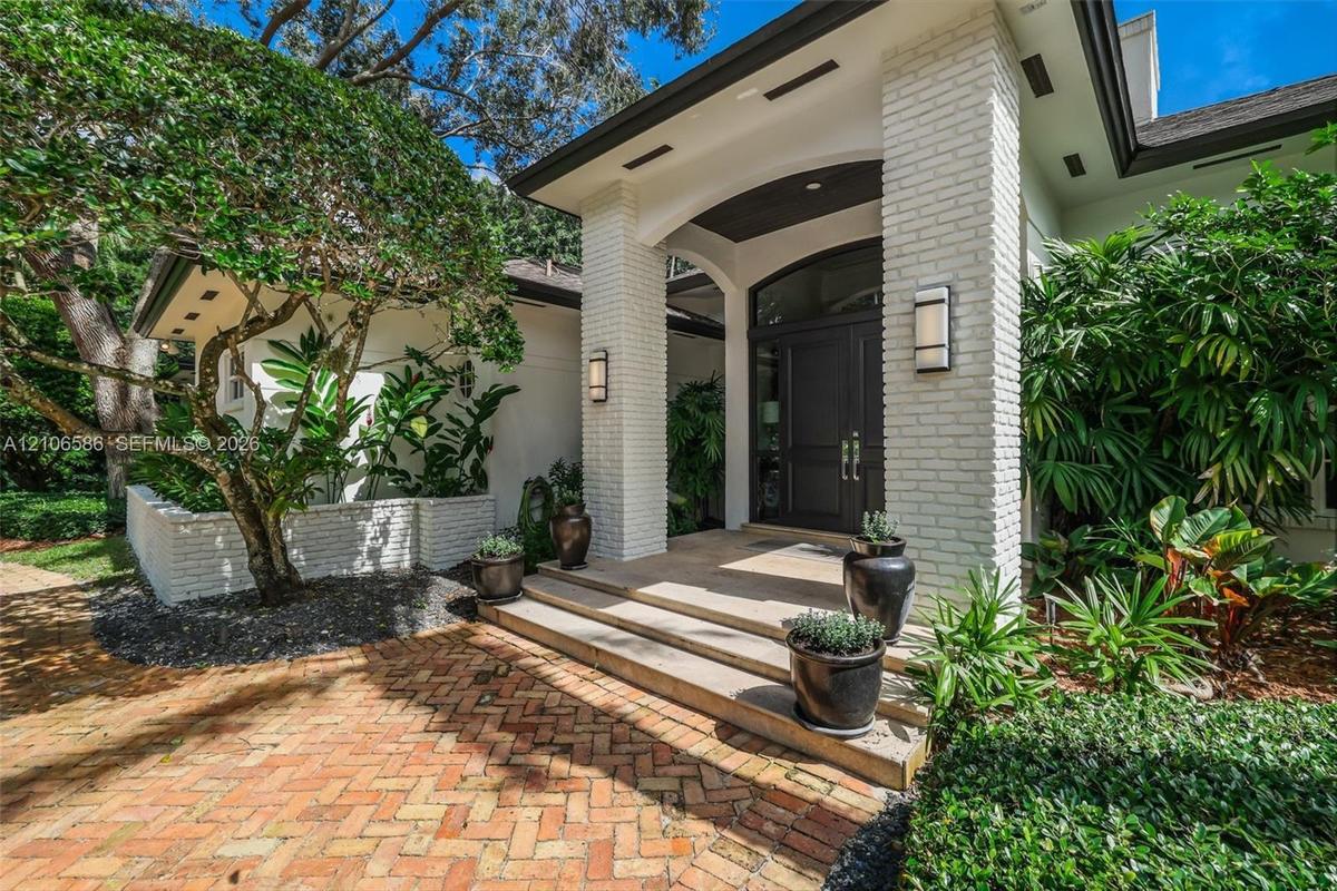 Covered entryway featuring white brick pillars, a multi-paneled dark wood front door with arched transom, tiered concrete steps, and a herringbone-pat