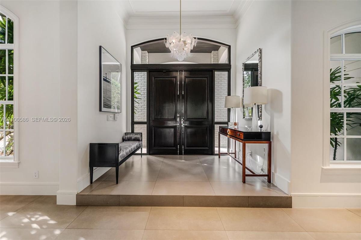 Foyer featuring large-format tile flooring, a set of double entry doors with transom window, oversized arched windows, and an ornate glass chandelier