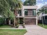 Contemporary two-story exterior featuring wood-finish siding, a private balcony with horizontal metal railings, a modern garage door, and a stone-pave