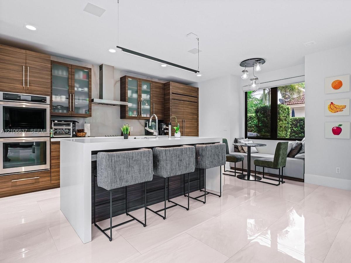Modern kitchen featuring horizontal-grain wood cabinetry, a central island with a waterfall-edge countertop, built-in double wall ovens, recessed ligh