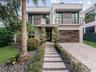 Contemporary two-story exterior featuring smooth stucco facade, horizontal wood-finish cladding, second-story balcony with metal railing, and paver wa
