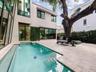 Exterior courtyard featuring an in-ground swimming pool with integrated steps, stone-tile decking, full-height floor-to-ceiling windows, and mature tr