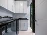 Glossy white cabinetry with vertical pulls, solid-surface dark countertop, undermount sink with gooseneck faucet, light-toned polished flooring, and f