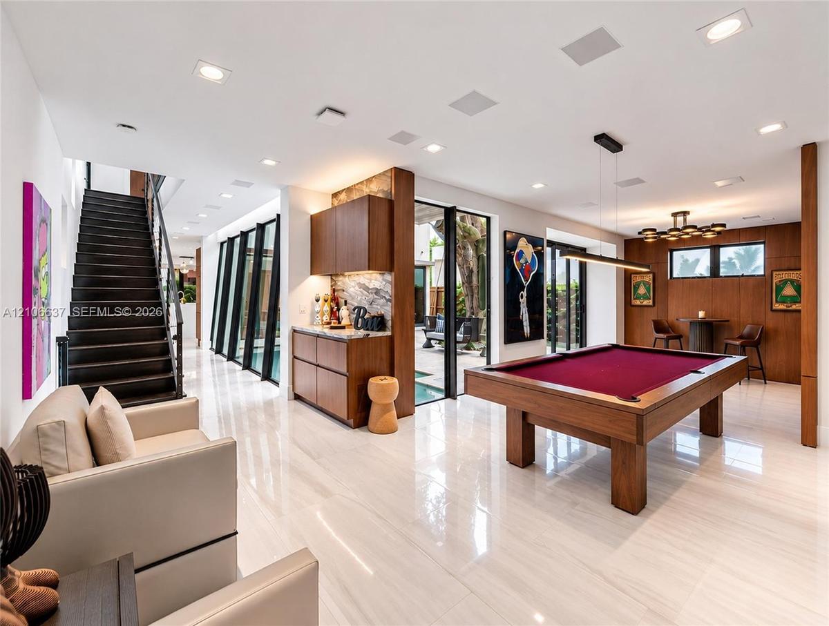 Polished stone flooring, wood-panelled accent walls, integrated bar cabinetry with stone backsplash, staircase with open risers, and floor-to-ceiling 