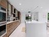 Contemporary kitchen featuring horizontal-grain wood cabinetry, expansive solid-surface island, stainless steel built-in double ovens, integrated stai