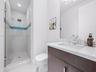 Modern bathroom featuring a dark wood-finish vanity, light-toned stone-finish countertop with an integrated rectangular sink, glass-enclosed shower wi