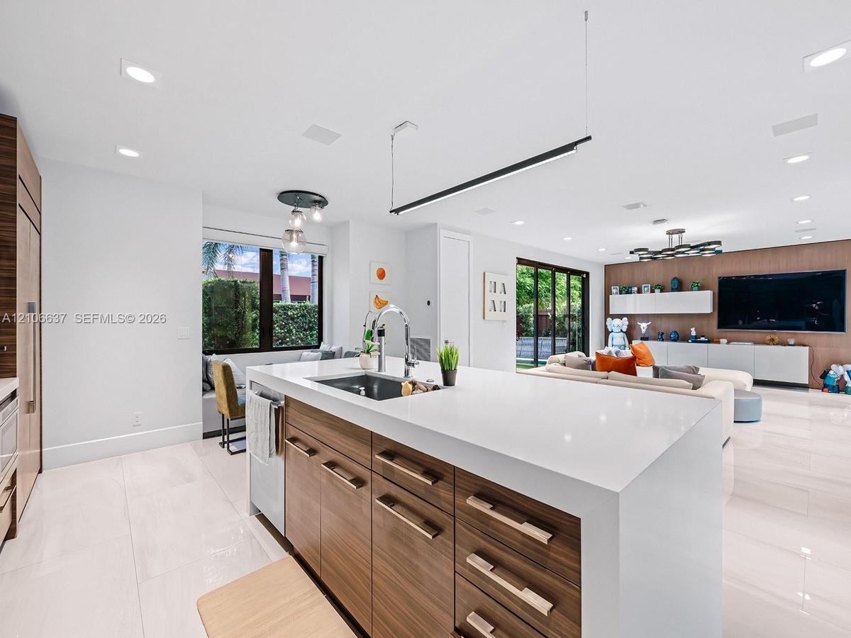 Kitchen island featuring a waterfall quartz countertop, undermount sink, integrated gooseneck faucet, and wood-finish cabinetry with metallic hardware