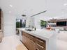 Kitchen island featuring a waterfall quartz countertop, undermount sink, integrated gooseneck faucet, and wood-finish cabinetry with metallic hardware