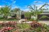 Single-story exterior featuring a tile roof, paved walkway, integrated multi-car garage, and professional landscaping with mature palms and diverse or