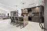 Kitchen featuring dark cabinetry, expansive stone-finish waterfall island, recessed lighting, dual pendant fixtures, and large-format tile flooring