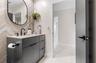 Modern vanity featuring charcoal cabinetry, a light-toned stone countertop, matte black fixtures, an arched wall mirror, and a herringbone-patterned t