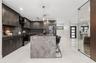 Kitchen featuring dark cabinetry, expansive stone-topped island, large-format tile flooring, stainless steel appliances, and glass-enclosed display ar
