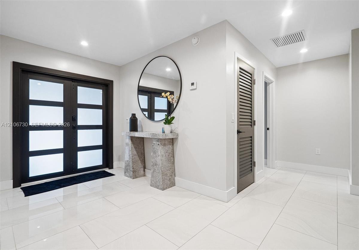 Entryway featuring double doors with frosted glass panels, large-format tile flooring, recessed ceiling lighting, and a built-in stone console table