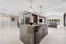 Kitchen island featuring a waterfall stone countertop, dark cabinetry, recessed lighting, and a glass-enclosed display storage unit