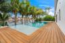 Waterfront swimming pool with an integrated spa, featuring wood-finish decking and mature palm trees