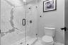 Walk-in shower featuring large-format stone-patterned tile, frameless glass enclosure, and matte black hardware, accompanied by a vitreous china toile
