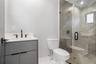 Modern vanity with a light-toned countertop, walk-in shower featuring full-height stone-finish wall tile, frameless glass enclosure, and matte black f