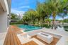 Waterfront backyard featuring a tiered wood-finish deck, an elevated pool with integrated spa, a built-in stone fire pit, and stone-surround hardscapi