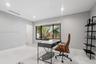 Modern home office featuring polished tile flooring, recessed ceiling lighting, and expansive multi-pane windows framing tropical landscaping