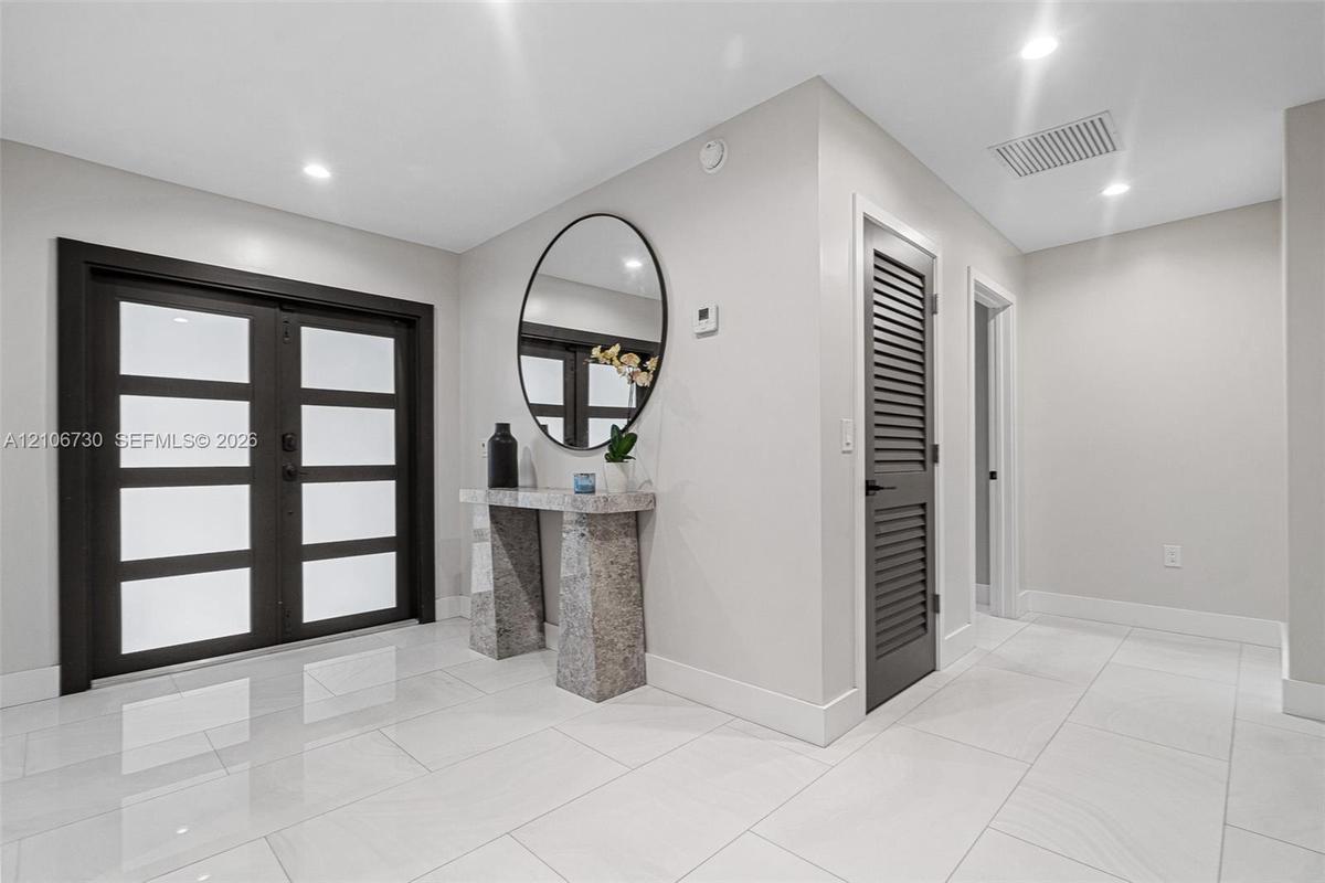 Foyer featuring double-entry doors with frosted glass panels, polished tile flooring, recessed lighting, and a louvered door