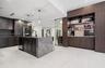 Kitchen featuring dark wood-finish cabinetry, a waterfall-edge stone island, built-in shelving with mirrored backsplash, and large-format tile floorin