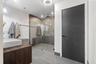 Bathroom featuring a wood-finish vanity with a white vessel sink, large-format tile flooring, a glass-enclosed walk-in shower, and a matte black hardw