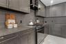 Kitchen featuring charcoal-toned cabinetry, solid-surface countertops with integrated backsplash, stainless steel gas range, black range hood, and lar