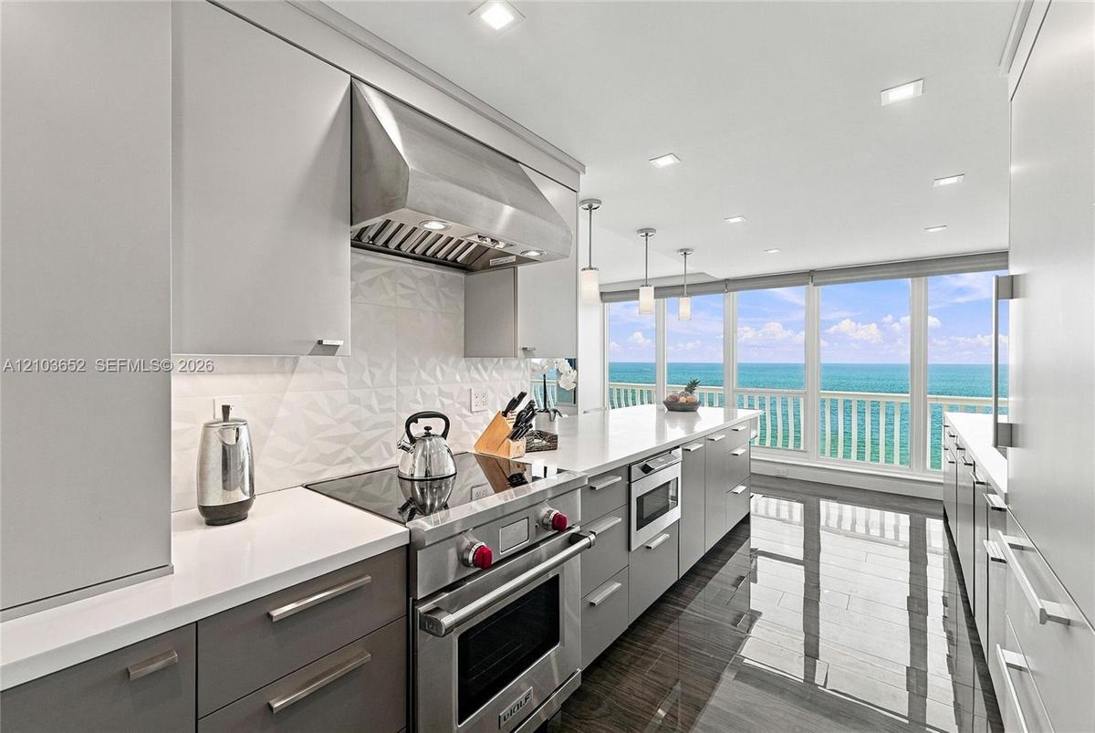 Modern kitchen featuring sleek two-tone cabinetry, professional-grade stainless steel range, geometric tile backsplash, stone countertops, and floor-t