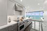 Modern kitchen featuring sleek two-tone cabinetry, professional-grade stainless steel range, geometric tile backsplash, stone countertops, and floor-t
