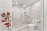 Walk-in shower featuring glass enclosure, ceiling-mounted rainfall showerhead, wall-mounted body sprays, built-in shelving, and floor-to-ceiling tile 